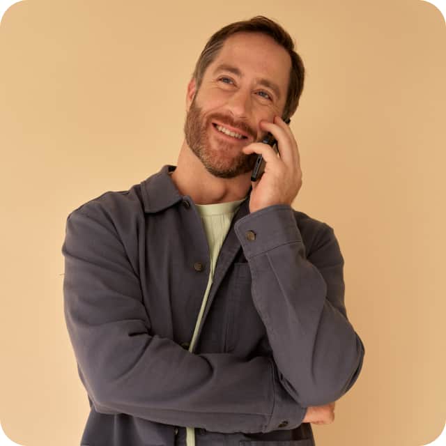 A casually dressed man engaged in a phone conversation, looking cheerful.